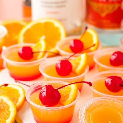 Close up photo of mai tai flavored jello shots on a what serving board garnished with maraschino cherries.