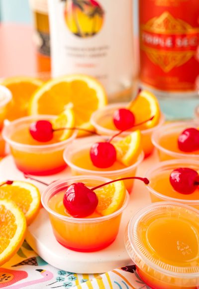 Close up photo of mai tai flavored jello shots on a what serving board garnished with maraschino cherries.