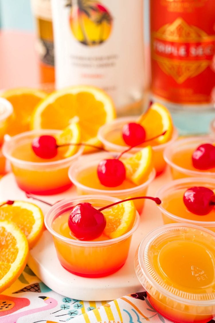 Close up photo of mai tai flavored jello shots on a what serving board garnished with maraschino cherries.