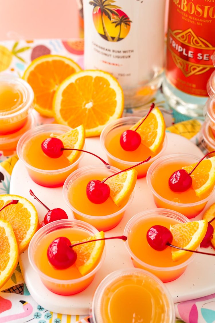 Close up photo of mai tai flavored jello shots on a what serving board garnished with maraschino cherries.