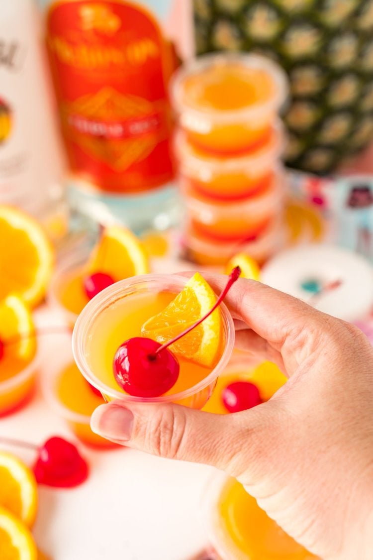 A woman's hand holding a mai tai jello shot to the camera.