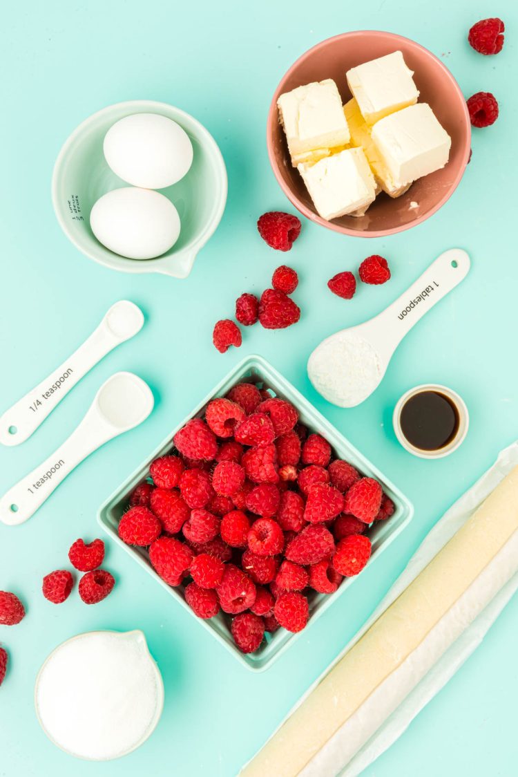 Ingredients to make raspberry danishes prepared on a blue surface.