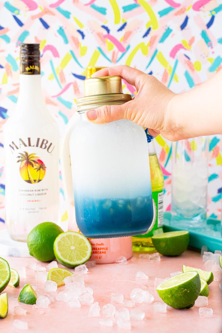 A cocktail being shaking in a blue and clear cocktail shaker.