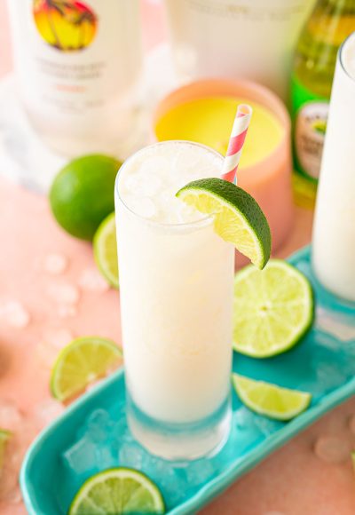 Close up of a RumChata Malibu Lime and Soda cocktail in a tall glass with limes around it.