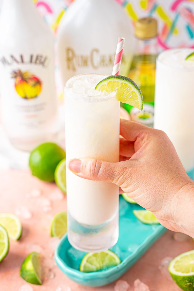 A woman's hand holding up a RumChata Malibu Lime and Soda cocktail to the camera.