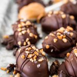 Close up photo of chocolate covered dates topped with chopped peanuts and flaky salt.