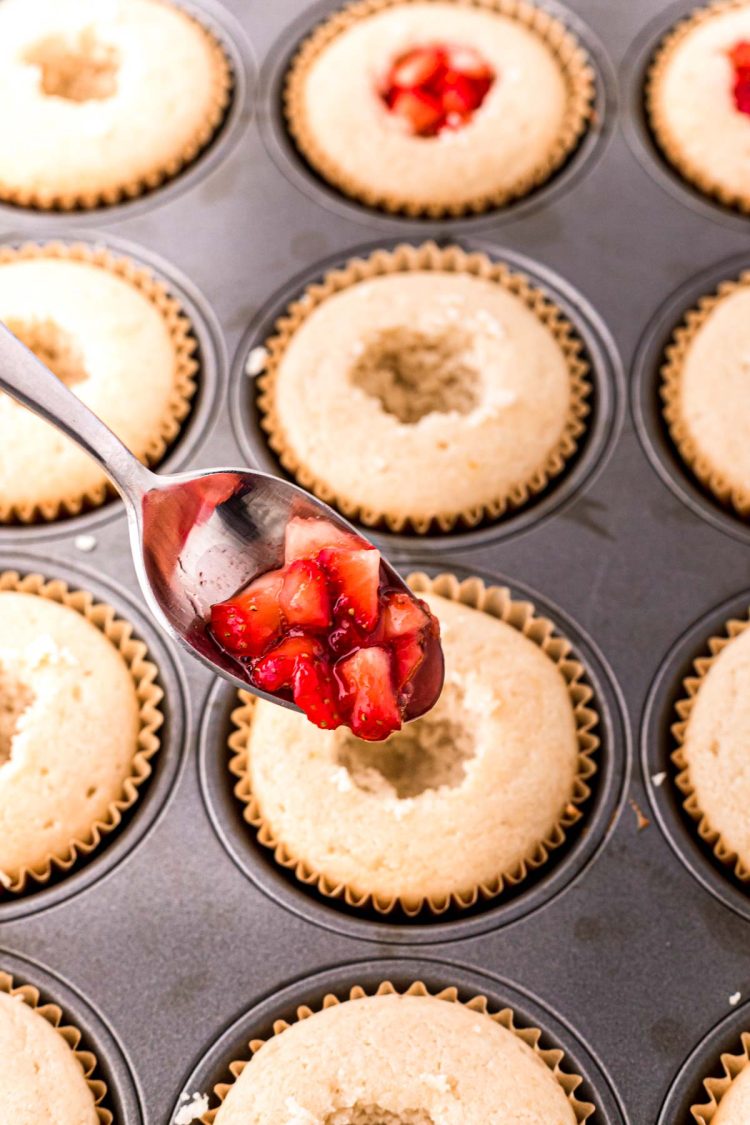 Strawberry filling being added to cored out vanilla cupcakes.