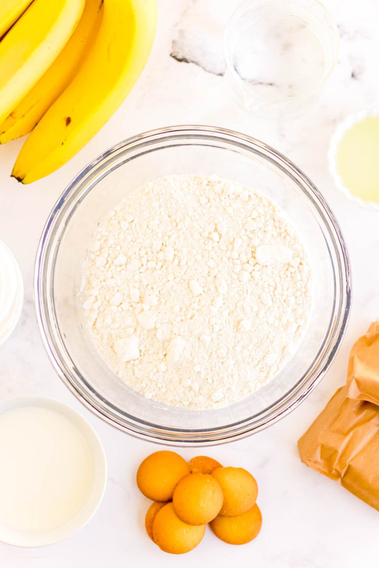 Ingredients to make banana pudding poke cake on a white surface.