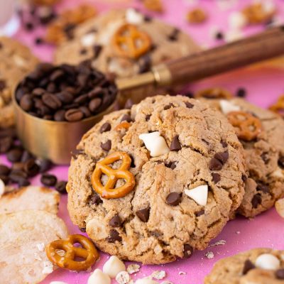 Compost cookies on a pink surface with ingredients all around them.