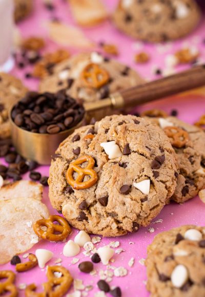 Compost cookies on a pink surface with ingredients all around them.