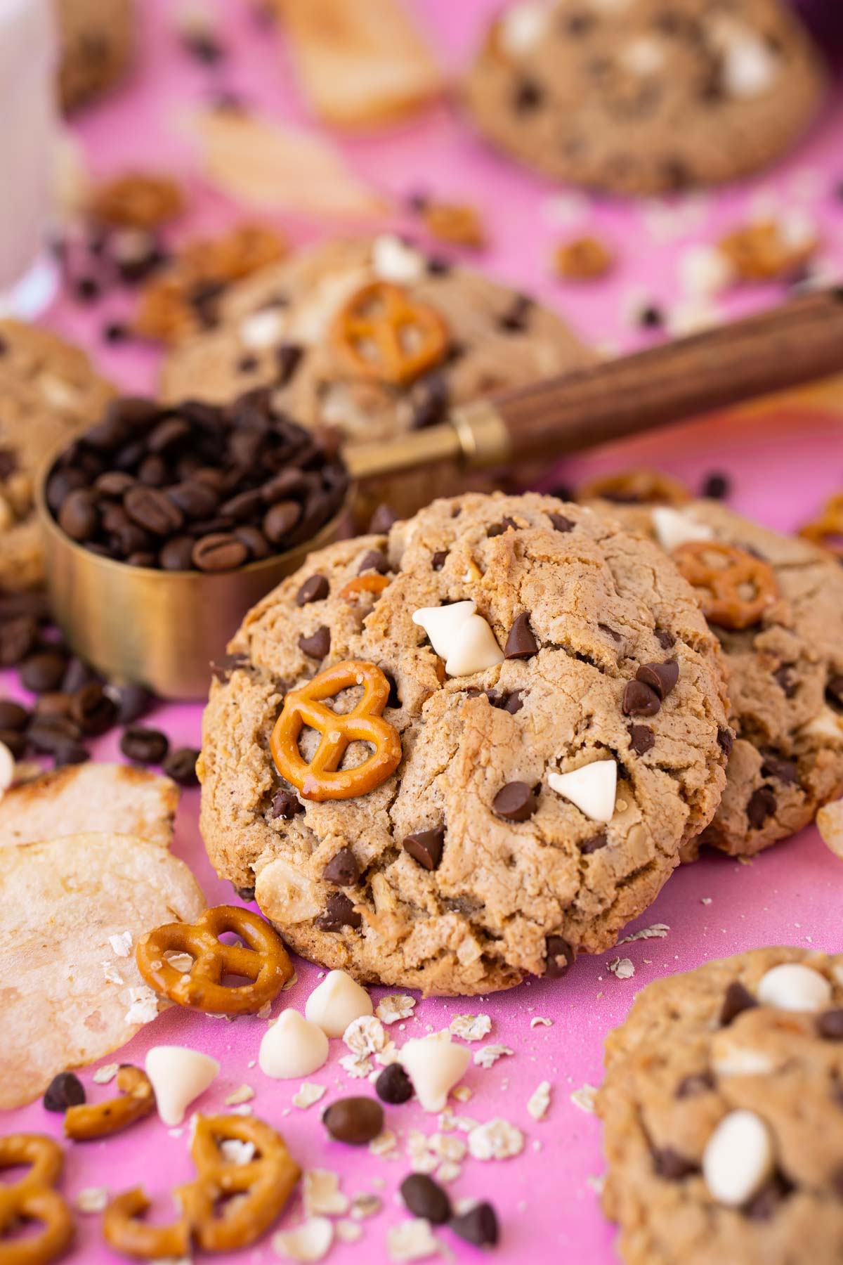 Compost cookies on a pink surface with ingredients all around them.