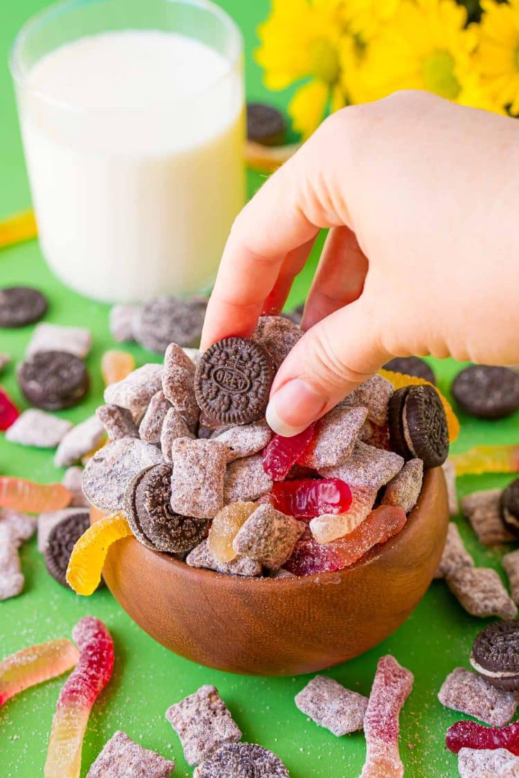 A womna's hand grabby some dirt cake muddy buddies from a wooden bowl.