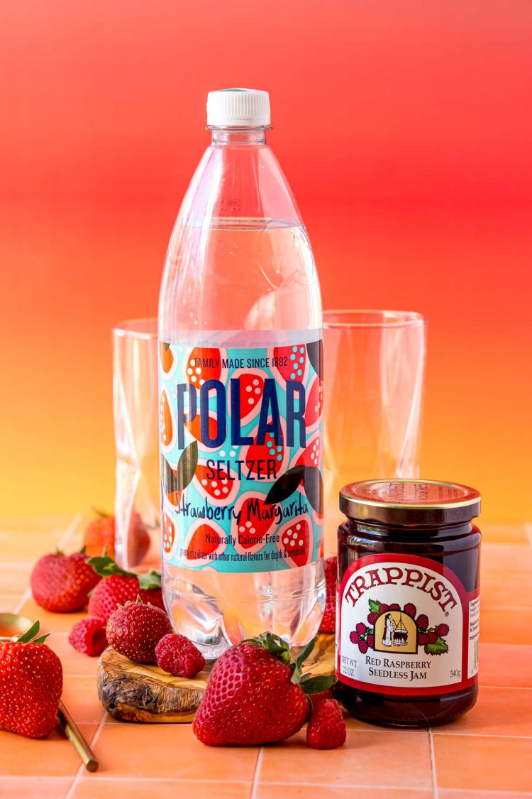 Ingredients to make jam and seltzer drink on an orange surface.