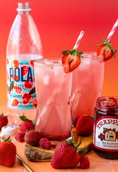 Jam seltzer drinks on a wooden board with raspberries and strawberries around them.