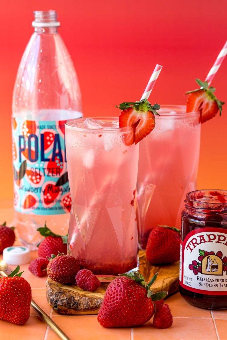 Jam seltzer drinks on a wooden board with raspberries and strawberries around them.