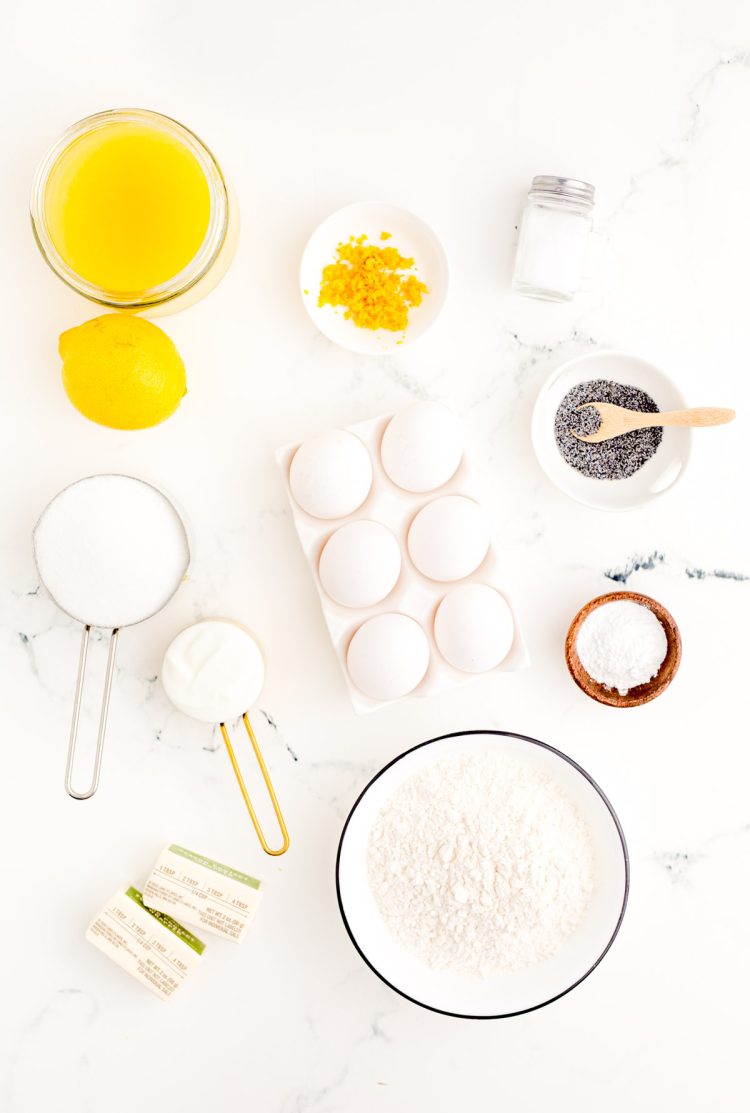 Ingredients to make lemon poppy seed muffins prepped on a marble surface.
