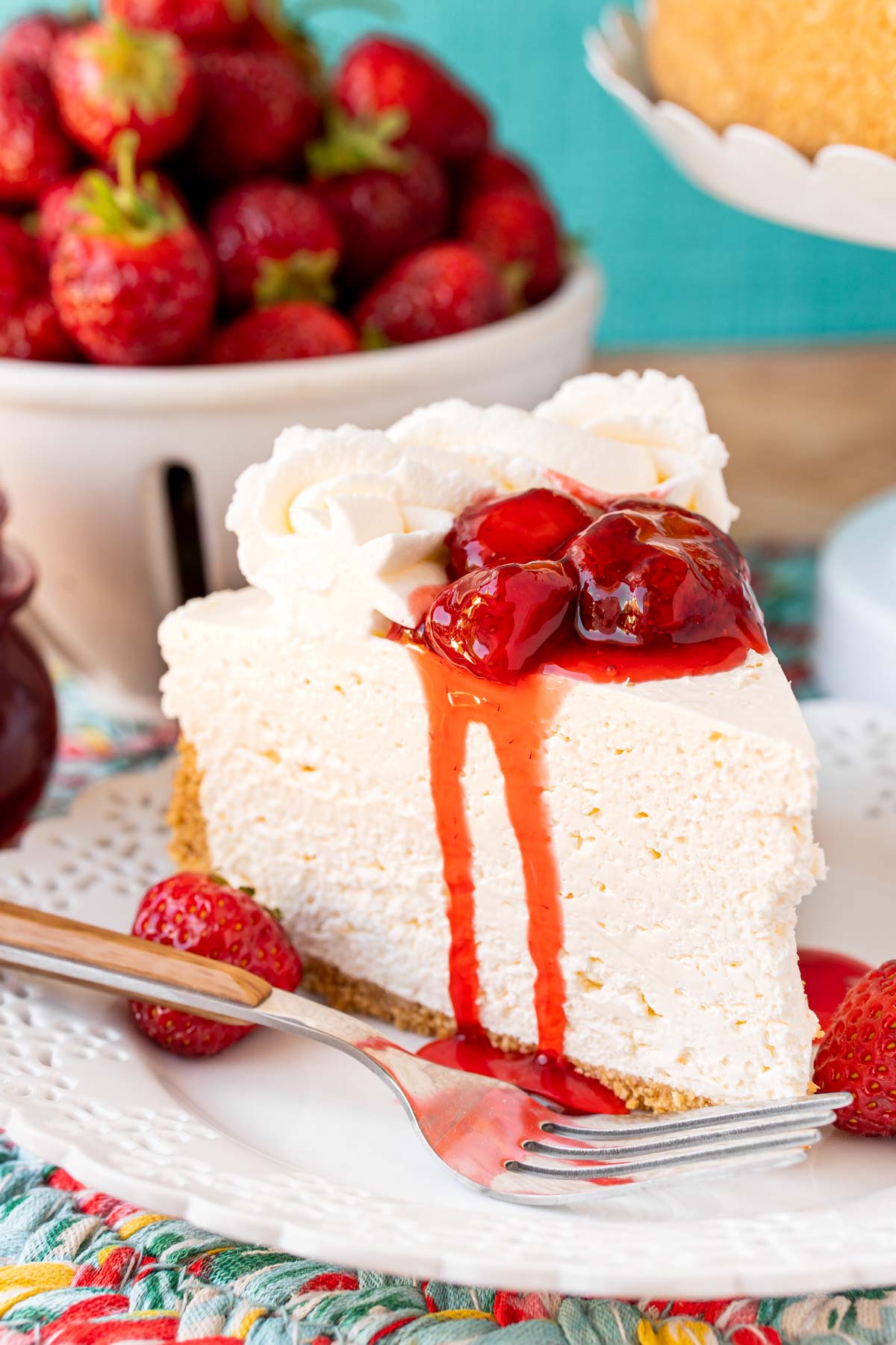 A slice of no bake cheesecake on a white plate topped with strawberry sauce and served with a fork.