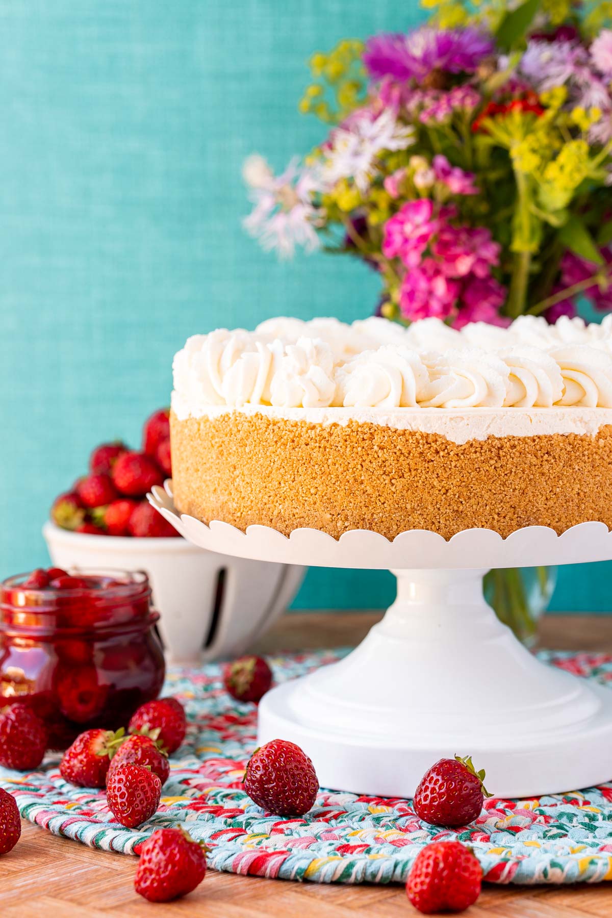 A no bake cheesecake on a white cake stand with strawberries and flowers in the background.