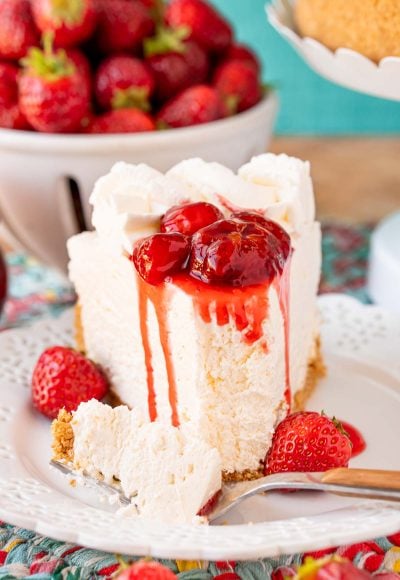A slice of no bake cheesecake on a white plate topped with strawberry sauce.