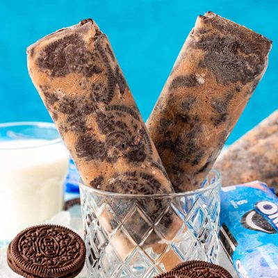 Close up photo of two Oreo popsicles in a glass with ice and oreos around it.