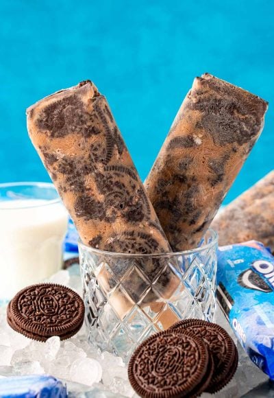 Close up photo of two Oreo popsicles in a glass with ice and oreos around it.