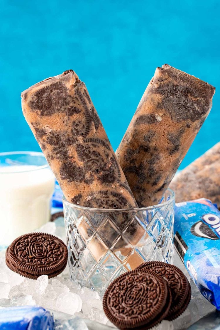 Close up photo of two Oreo popsicles in a glass with ice and oreos around it.