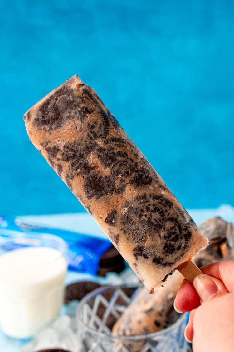 A woman's hand holding a cookies and cream popsicle to the camera.