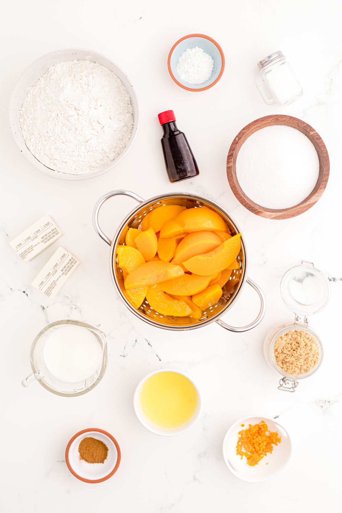 Ingredients to make peach cobbler prepped on a marble counter.