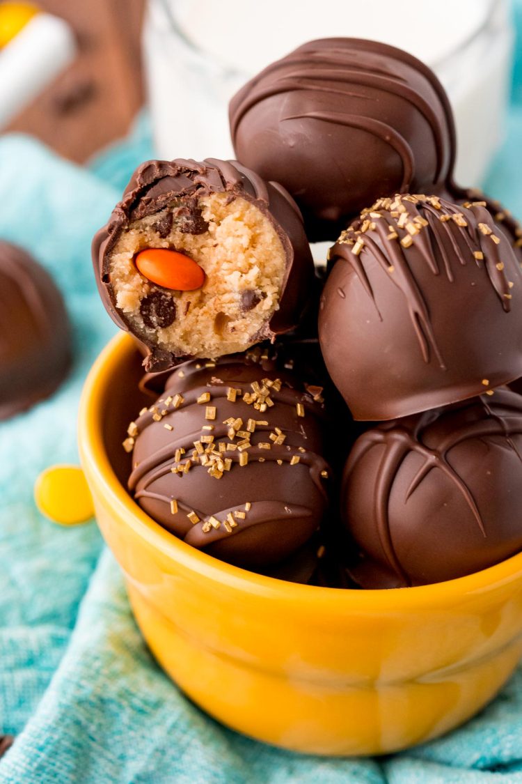 Close up photo of peanut butter cookie dough truffles in a yellow bowl, one truffle has a bite taken out.