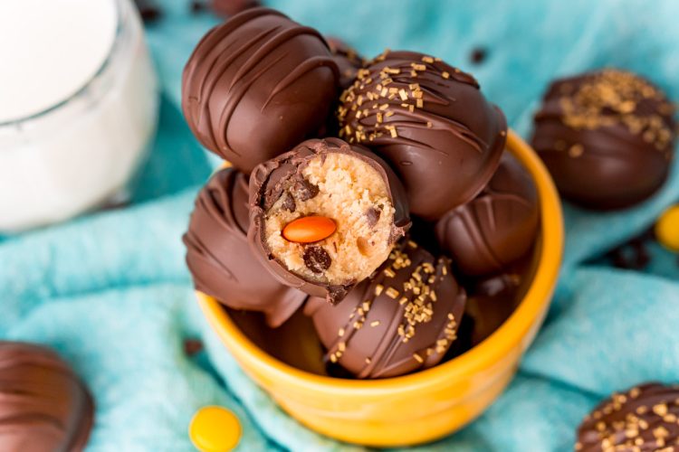 Close up photo of peanut butter cookie dough truffles in a yellow bowl, one truffle has a bite taken out.