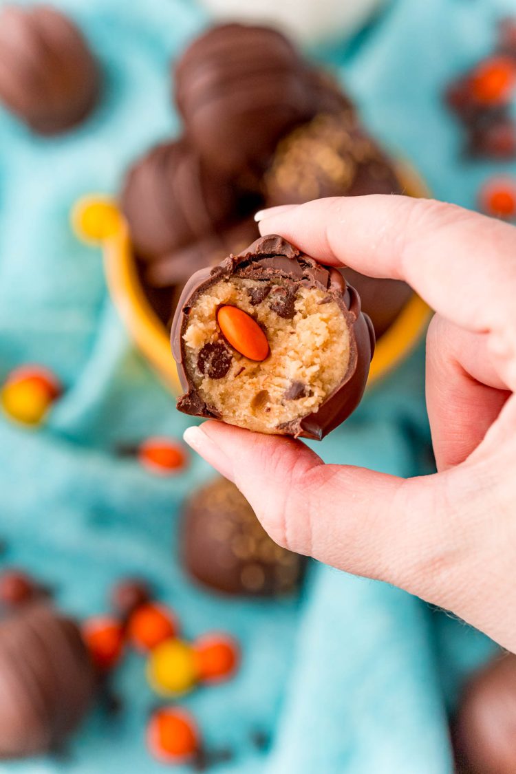 A woman's hand holding a peanut butter cookie dough truffle with a bite taken out of it.