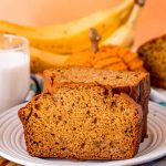 Close up of a slice of pumpkin banana bread on a plate leaning against a stack of other slices.