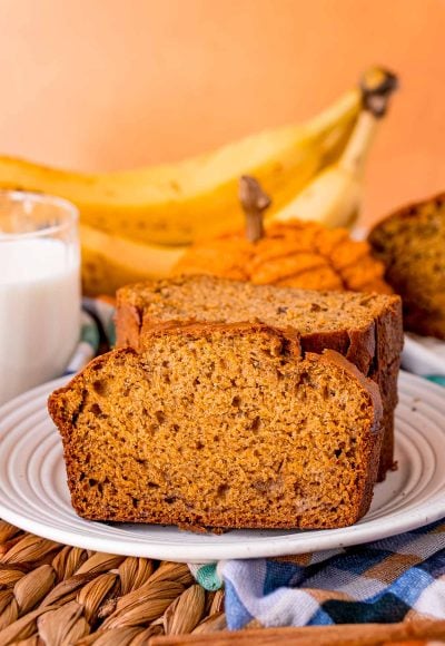 Close up of a slice of pumpkin banana bread on a plate leaning against a stack of other slices.