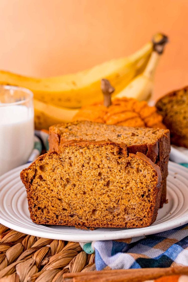 Close up of a slice of pumpkin banana bread on a plate leaning against a stack of other slices.