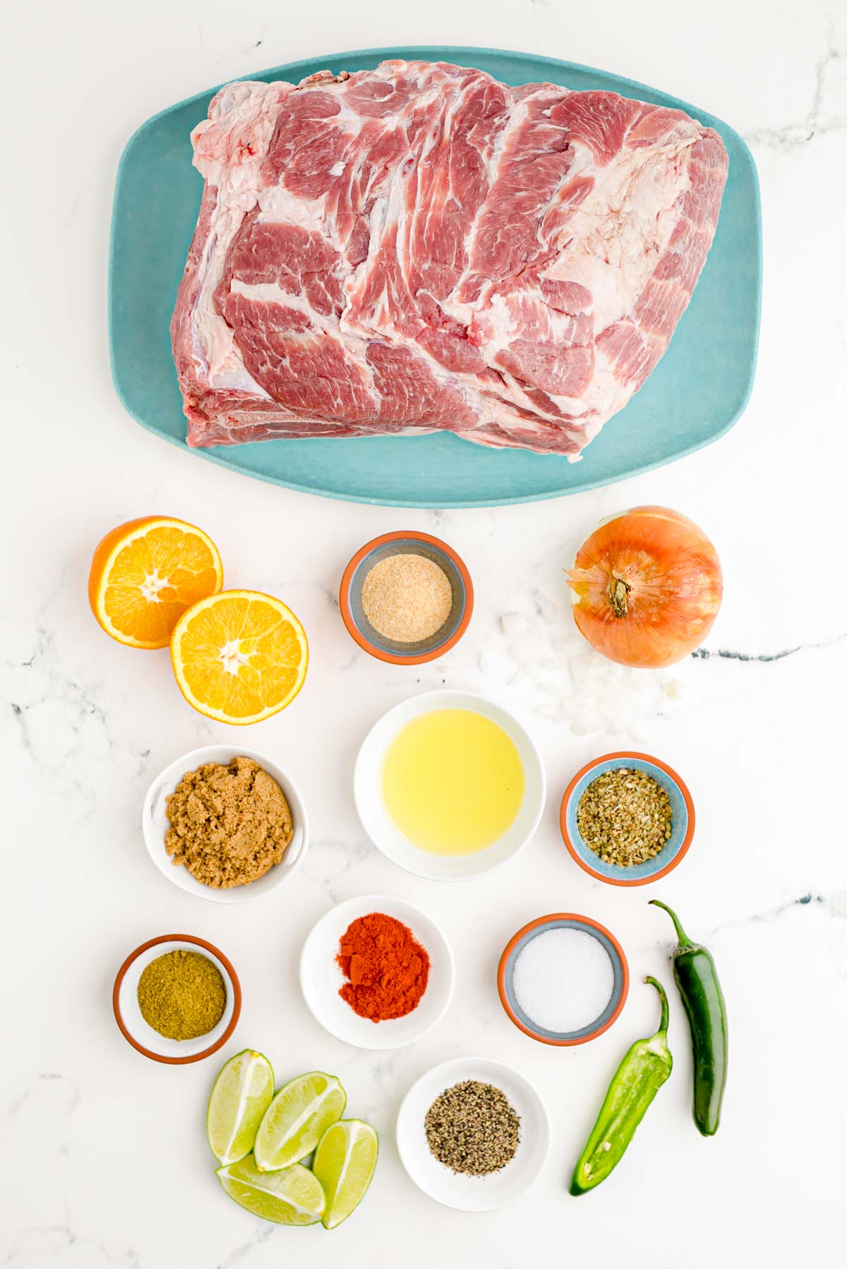 Ingredients to make pork carnitas on a marble surface.