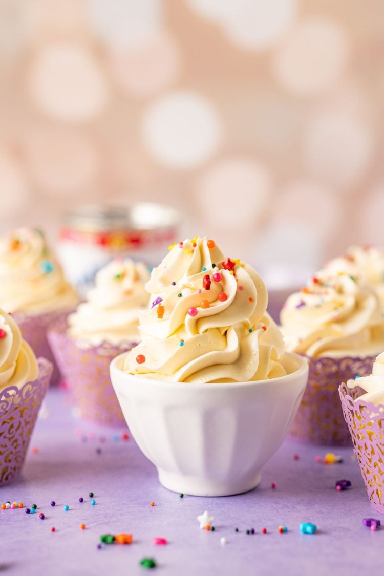 Sweetened condensed milk frosting in a white bowl with cupcakes around it.