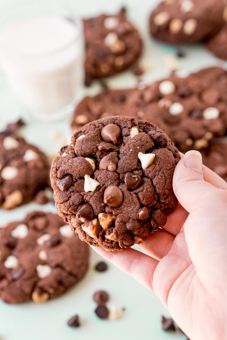 A woman's hand holding a triple chocolate chip cookie to the camera.