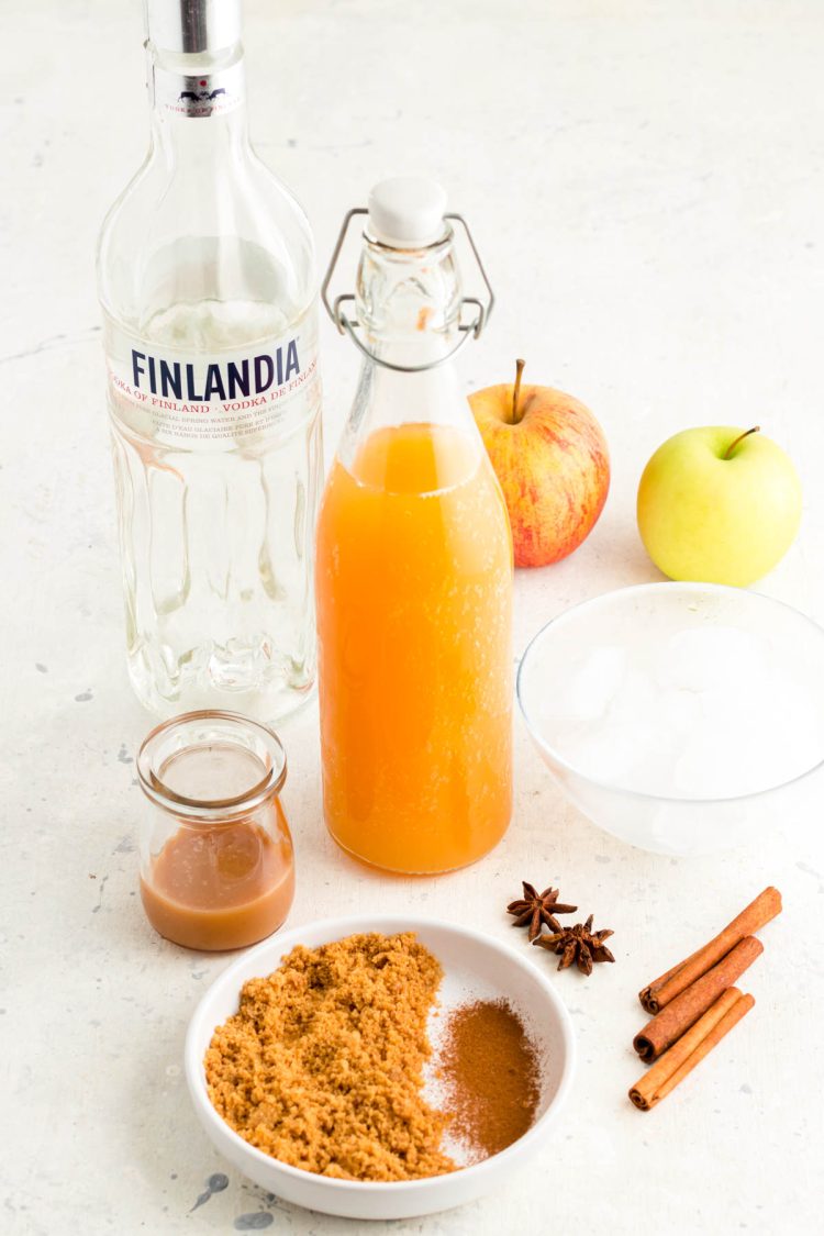 Ingredients to make an apple cider martini on a white table.