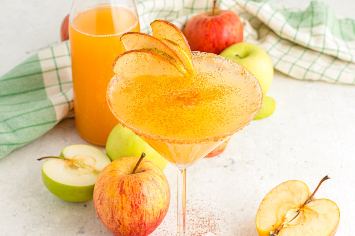 Close up pf an apple cider martini on a white table with a green napkin.
