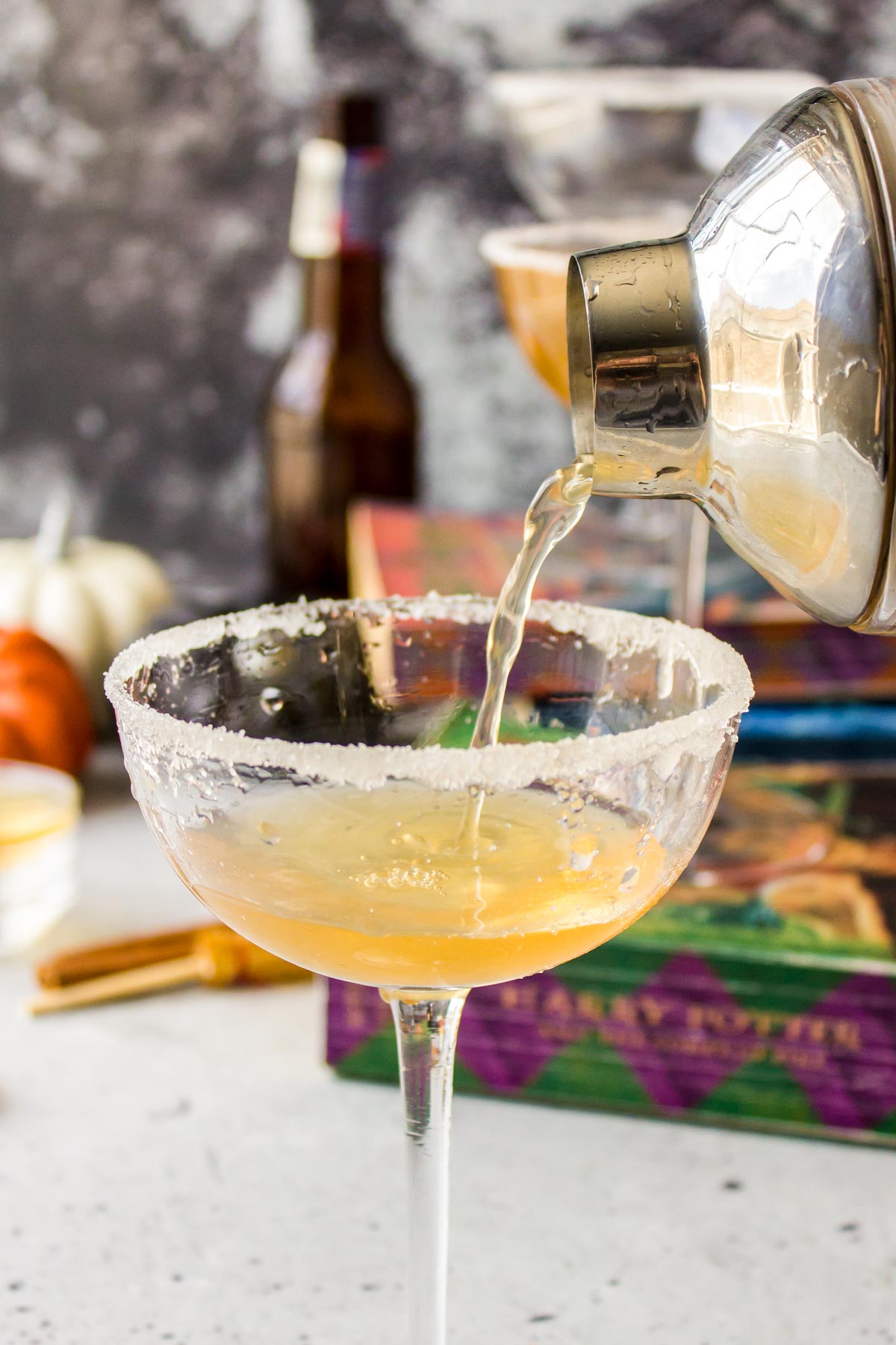 A butterbeer cocktail being poured into a coupe glass.