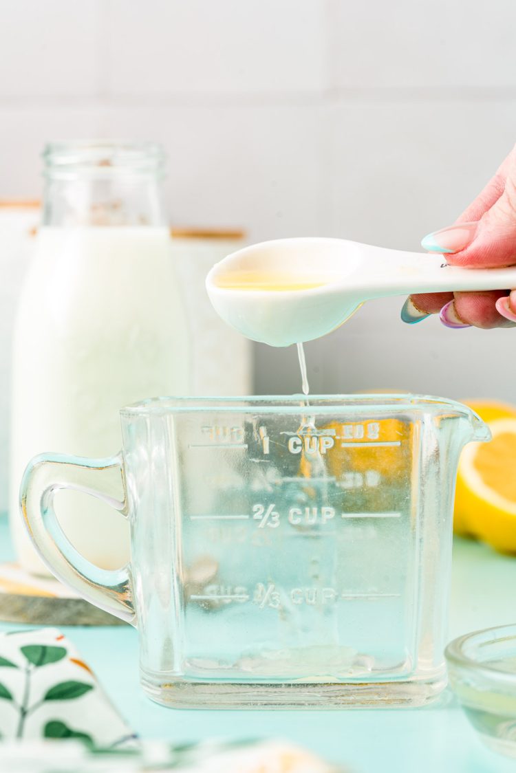 Lemon juice being added to a glass measuring cup with a measuring spoon.