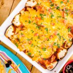 Overhead photo of chicken enchiladas in a baking dish on a wooden table.