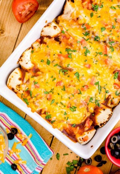 Overhead photo of chicken enchiladas in a baking dish on a wooden table.
