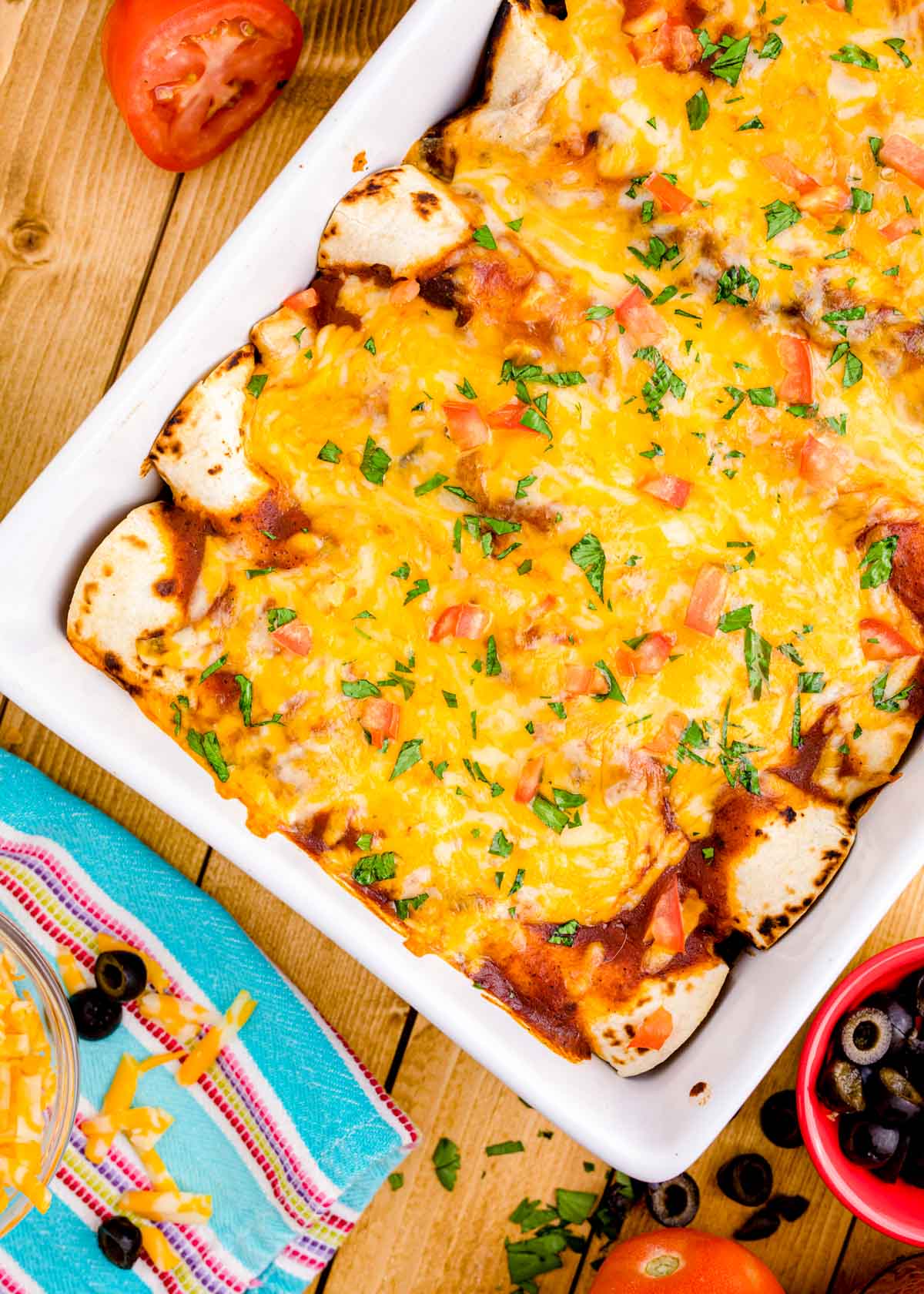 Overhead photo of chicken enchiladas in a baking dish on a wooden table.