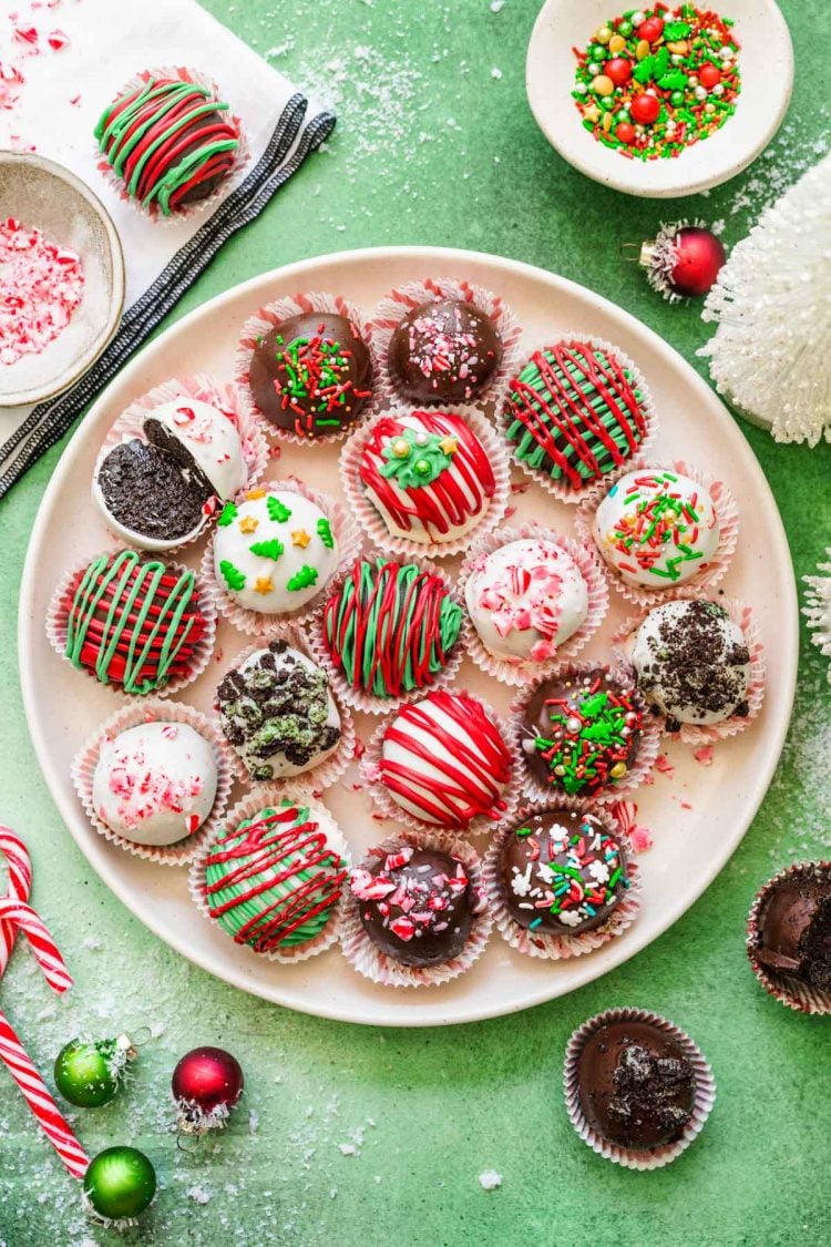 Christmas Decorated Oreo Balls on a white plate on a green surface.