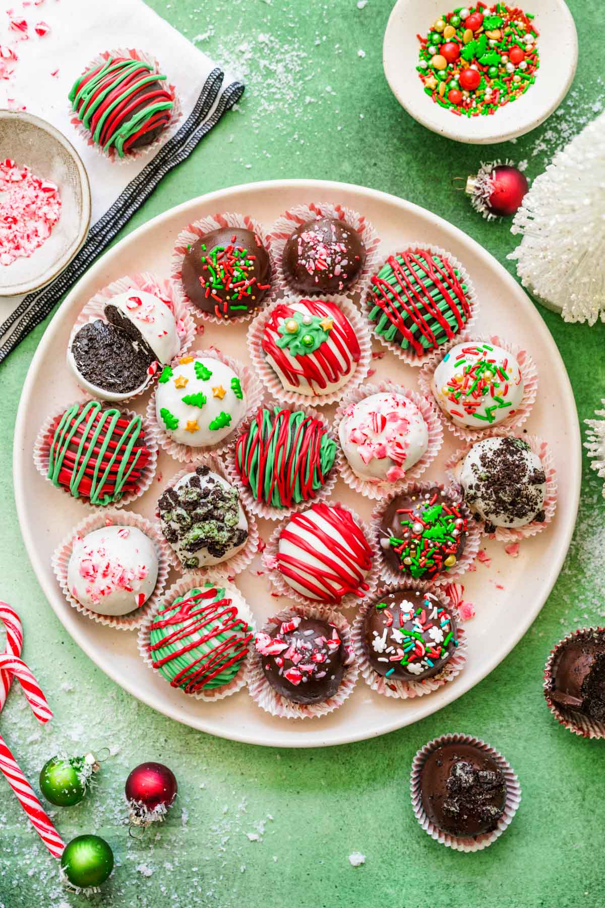 Christmas Decorated Oreo Balls on a white plate on a green surface.