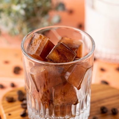 Coffee ice cubes in a glass with coffee beans scattered around it.