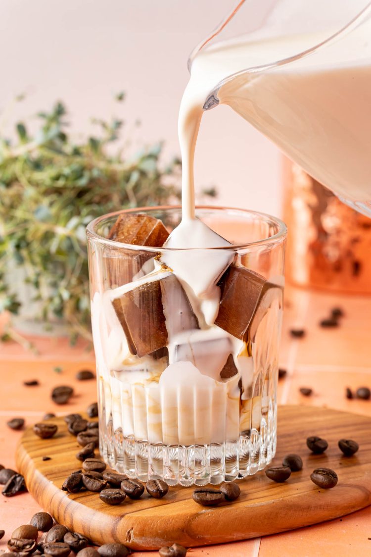 A small pitcher pouring milk into a glass with coffee ice cubes.