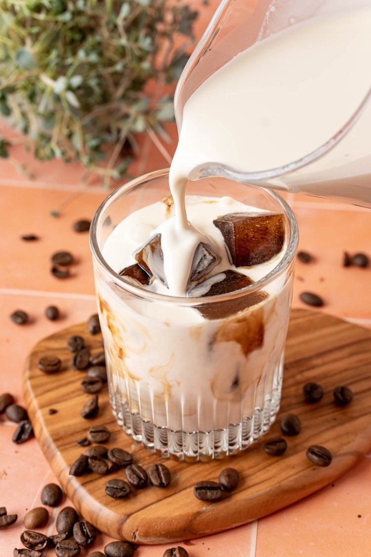 Cream being poured into a glass over coffee ice cubes.