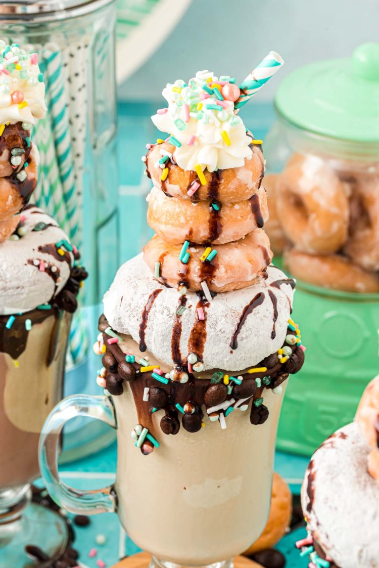 A mug of coffee milkshake topped with donuts and whipped cream and sprinkles.